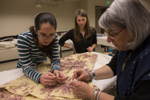 Graduate intern Rachel Crooks, left, works with volunteer Alana Eisemann and Dr. Susan Tontore on a French textile that dates back to 1820.