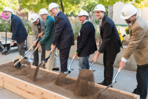 seven people with shovels and hardhats turning over soil in a groundbreaking ceremony