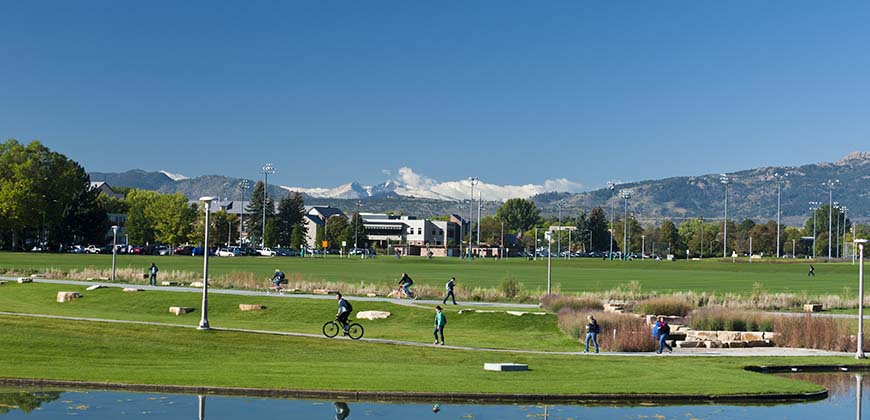 Students walk on the West Lawn of the Colorado State University in the with snow on Longs Peak in the background and the Lagoon in the foreground.