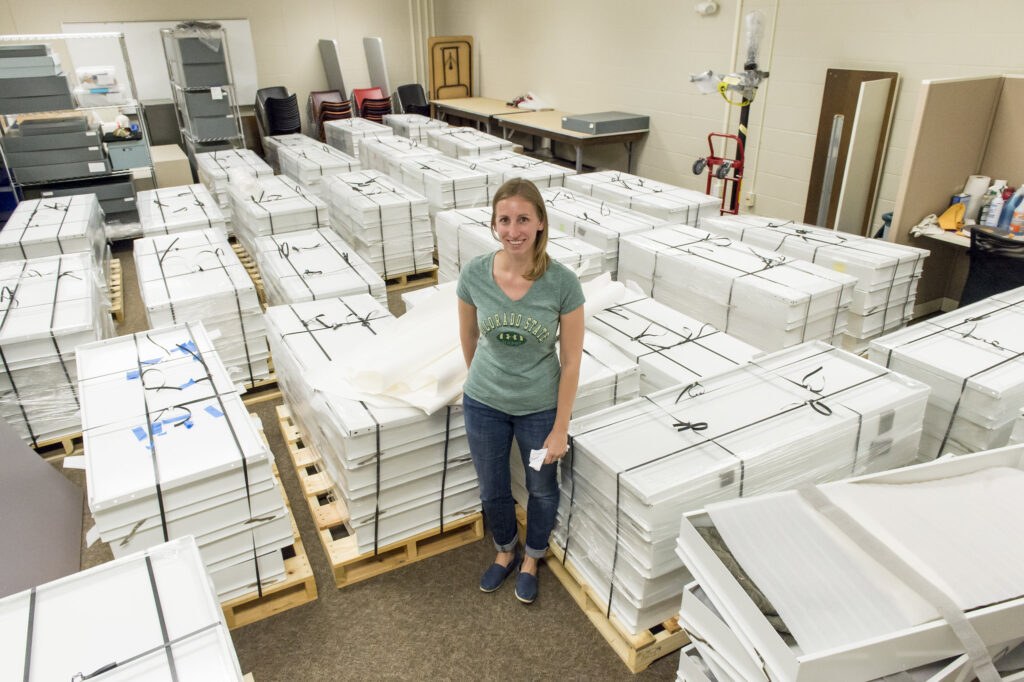 A woman standing in a room filled with packed flat boxes on palettes.