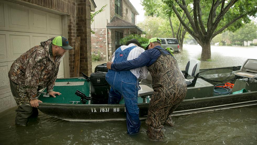Two men help elderly man into boat in flooded driveway