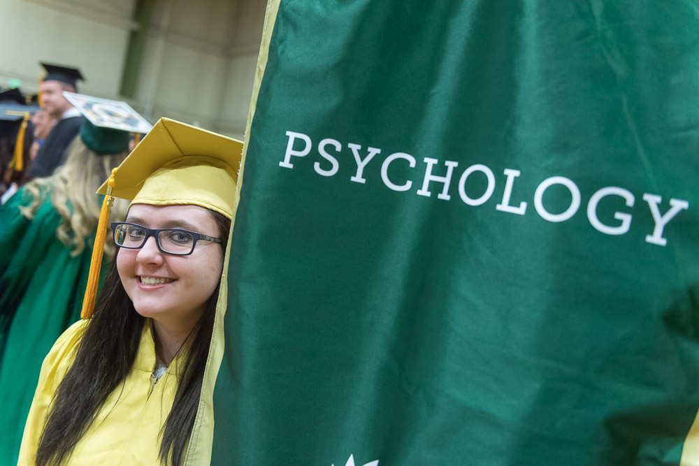 Female graduate in yellow gown with Psychology banner