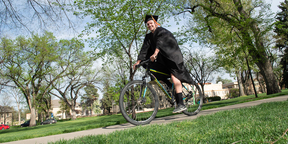 Grad in cap and gown rides bike on Oval