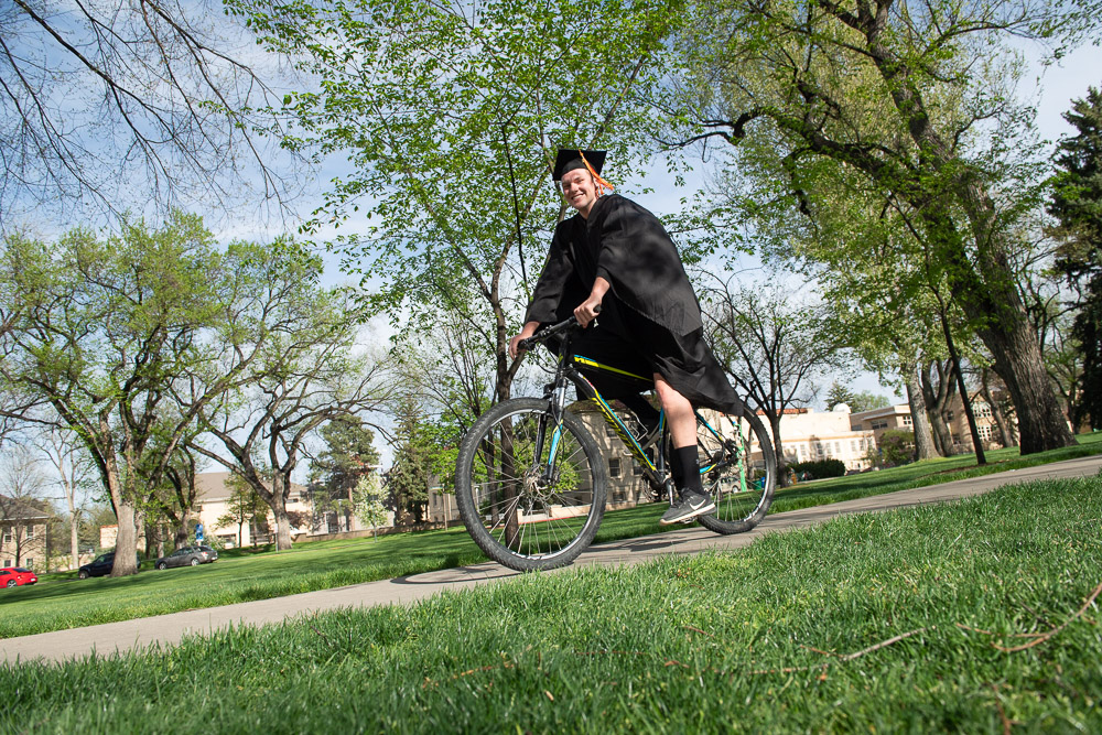 Grad in cap and gown rides bike on Oval