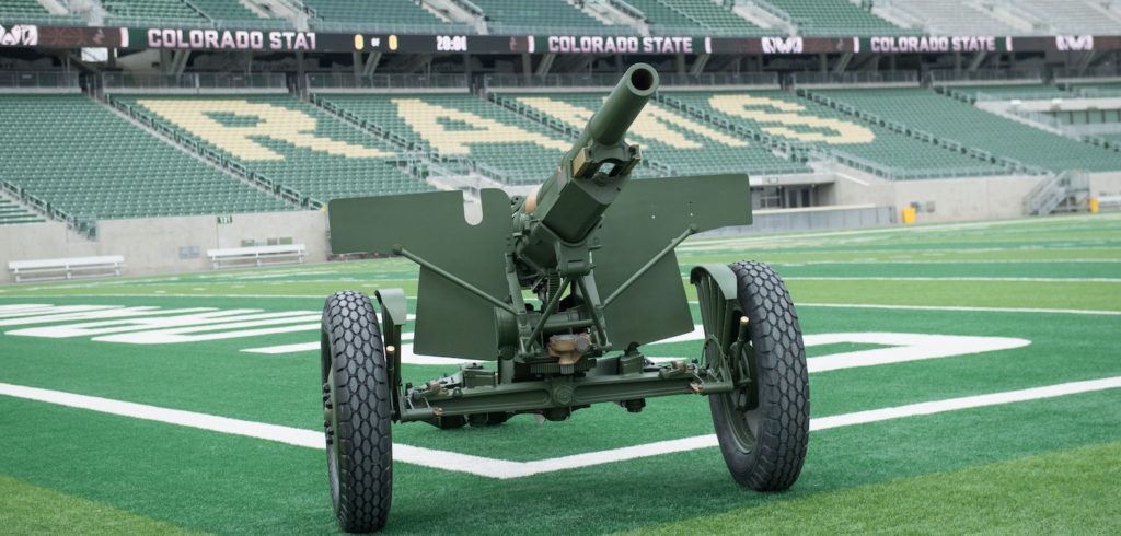 CSU's restored cannon sits in on a football field. The cannon is a Word War One era French Howlitzer field gun. It is green with two large wheels affixed to the base.