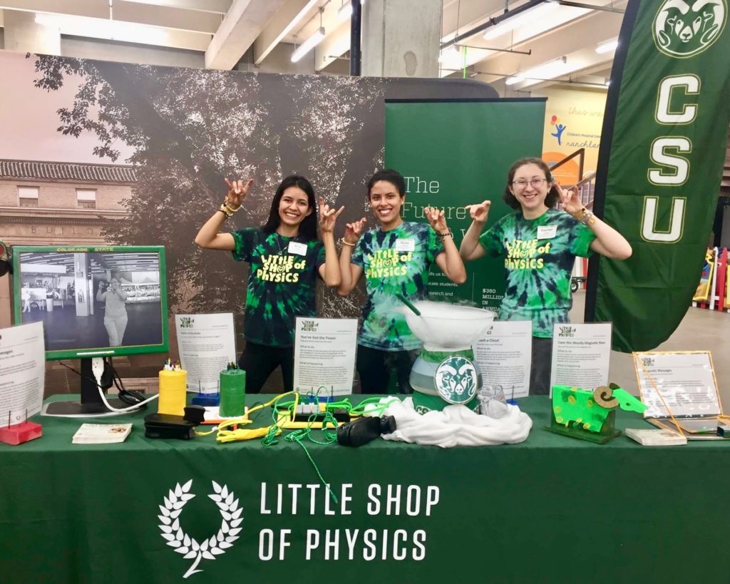 Three team members from the CSU Little Shop of Physics smiling at CSU's booth at the 2018 Denver County Fair.