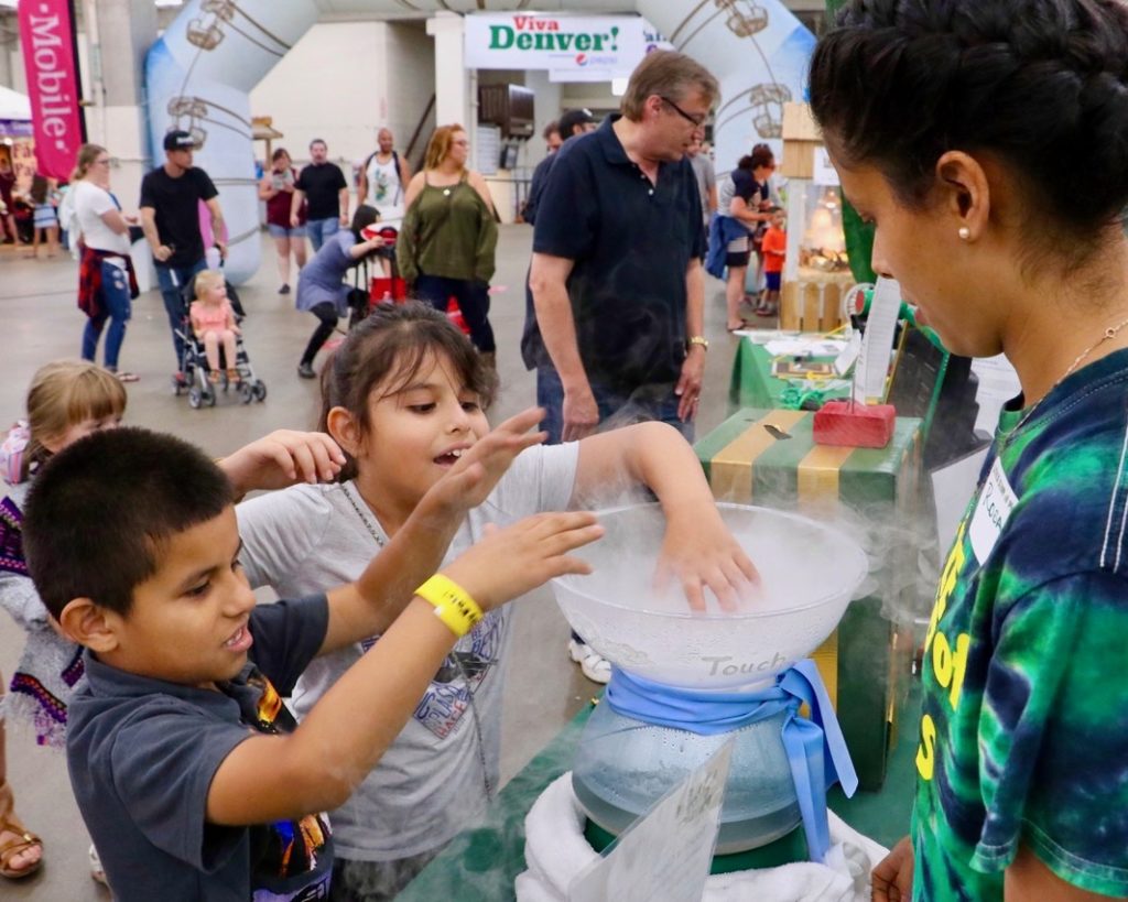 CSU Little Shop of Physics volunteer guides two young children through experiment at CSU's booth at the 2018 Denver County Fair.