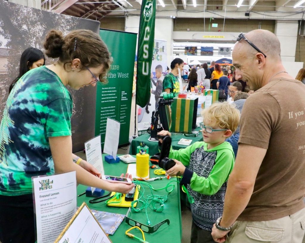 CSU Little Shop of Physics volunteers guide young boy and father through experiment at CSU's booth at the 2018 Denver County Fair.