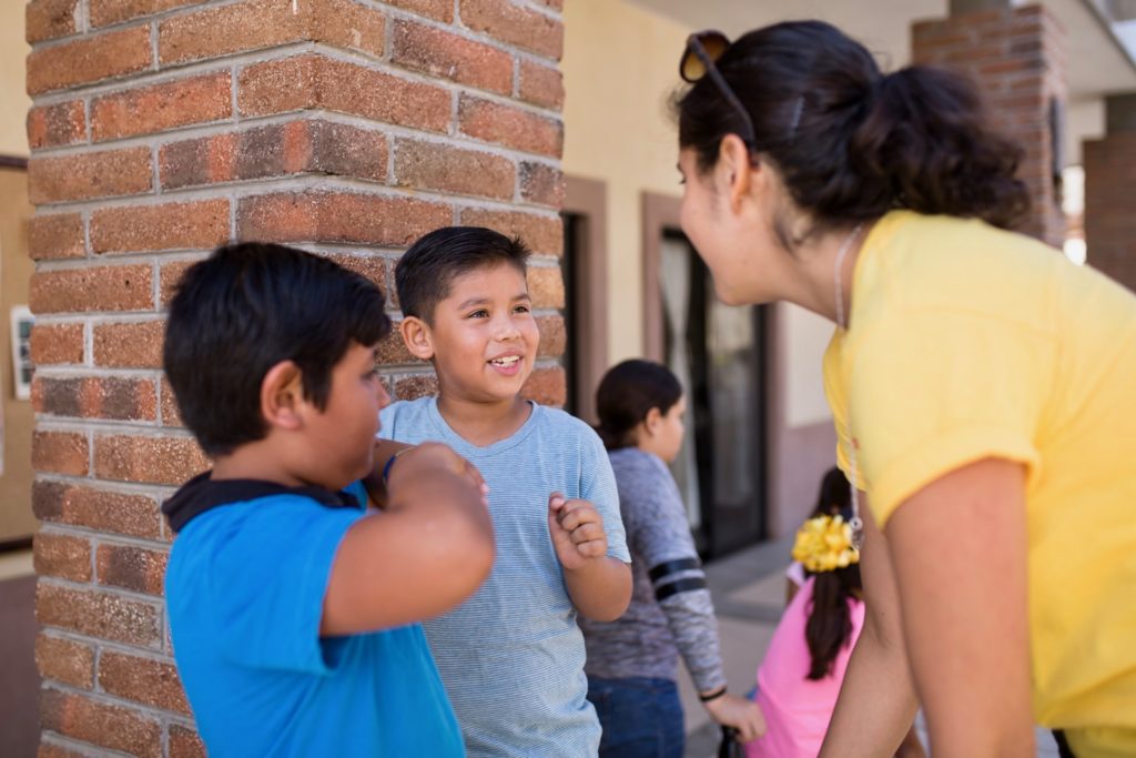 Kids Do It All instructor speaking with two young participants next to brick pillar at CSU Todos Santos Center.