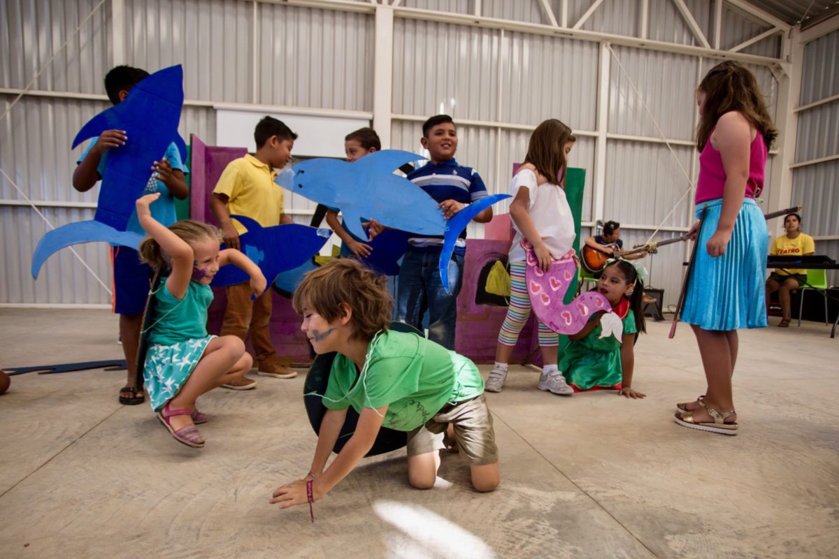 Group of youth participating in the Kids Do It All program at the CSU Todos Santos Center smile and dance while holding ocean-themed props during youth music-theatre performance.
