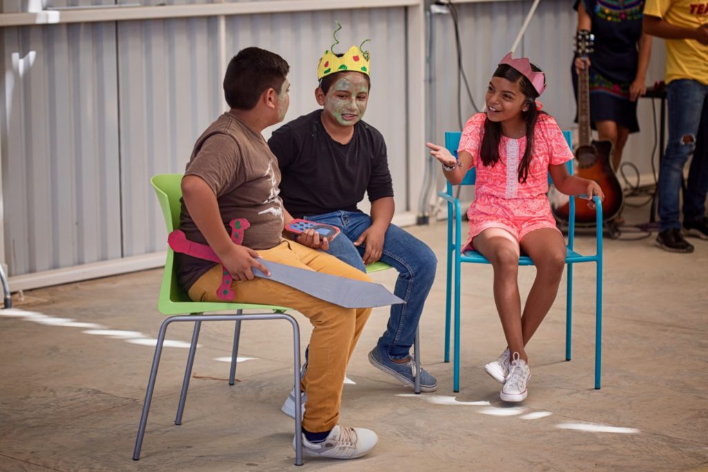 Three youth participating in the Kids Do It All program converse in front of crowd at the CSU Todos Santos Center during music-theatre performance.
