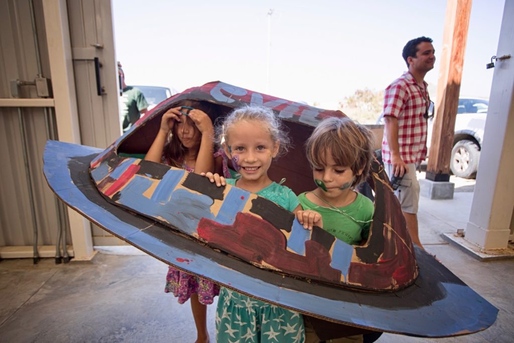 Three youth participating in the Kids Do It All program at the CSU Todos Santos Center smile inside papier-mâché UFO.