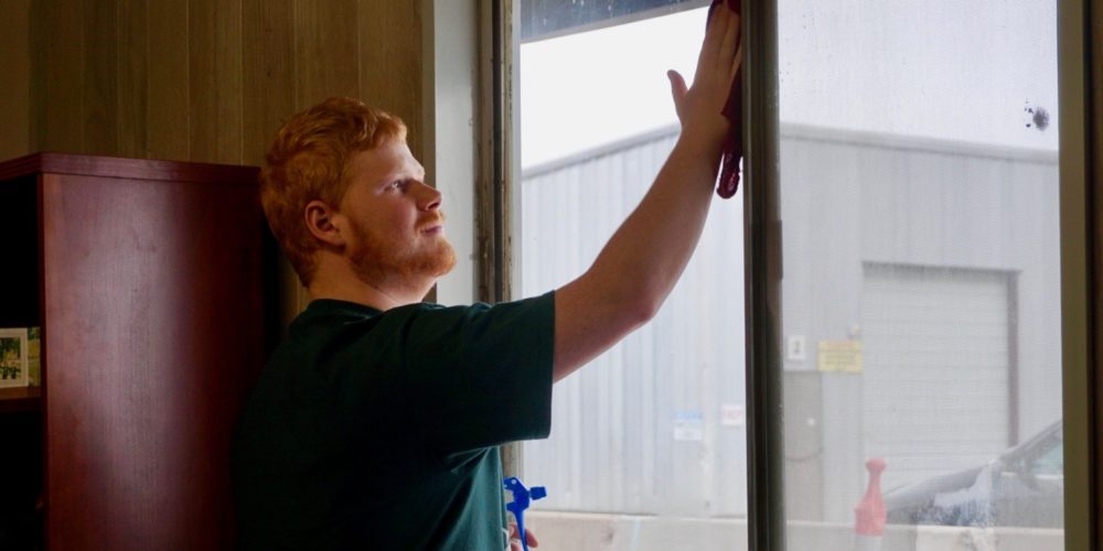Michael McGrady cleans window while smiling at the CSU Temple Grandin Equine Center.