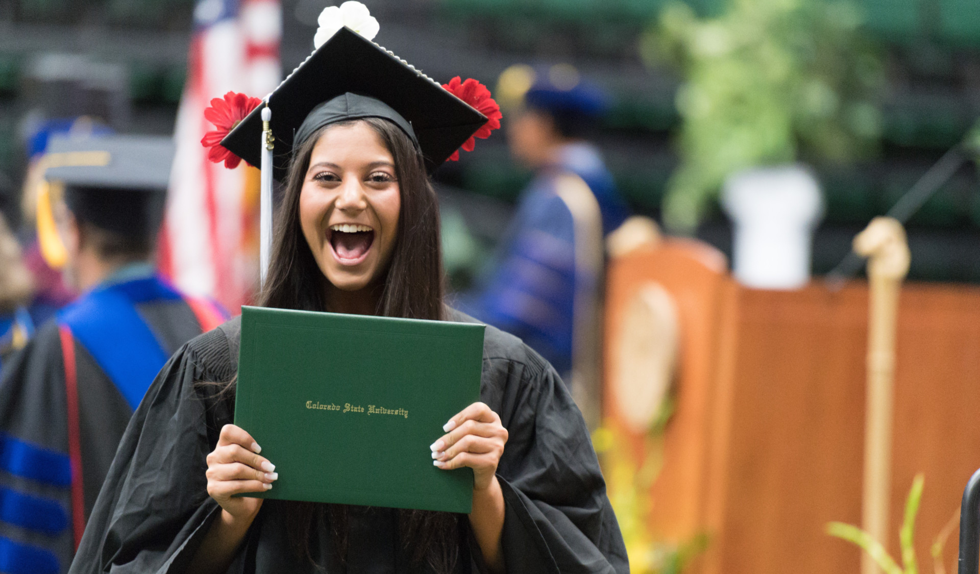 A happy student holding her diploma at a CSU commencement ceremony.