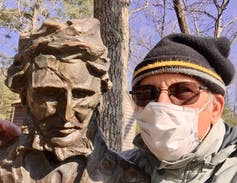 Man wearing mask next to statue of Thoreau