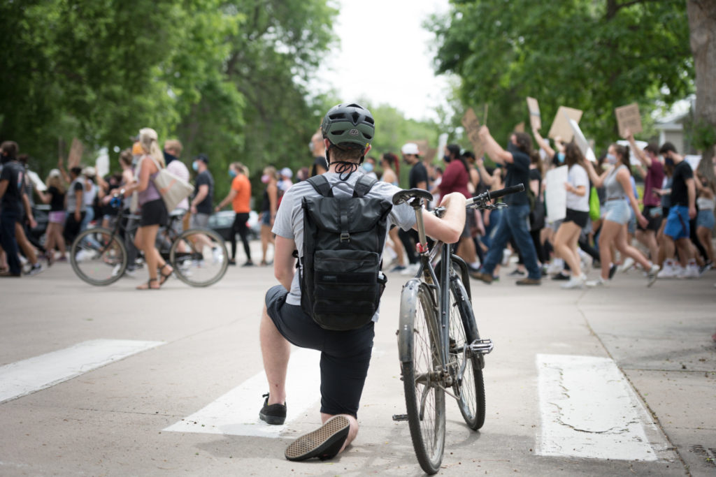Bicyclist kneeling as march crosses street