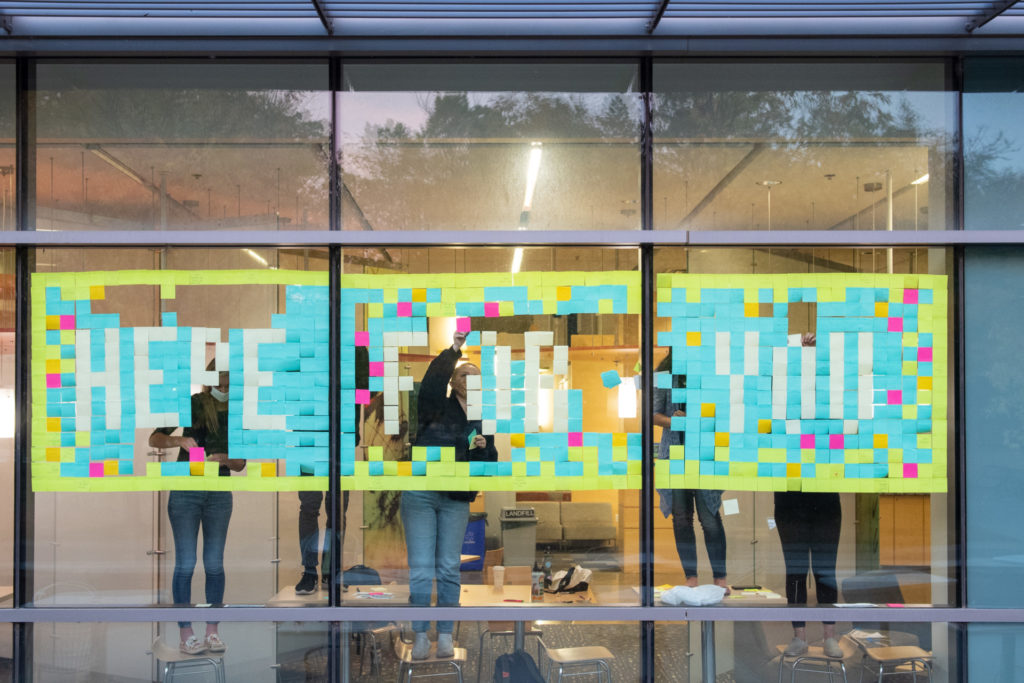 Members of Active Minds at Colorado State University create a mural of sticky notes spelling out "Here For You," the club's slogan, and hand-written positive messages, October 21, 2020, on a window in the Behavioral Sciences Building. Active Minds at CSU is a mental health advocacy organization that seeks to empower college students to speak openly about mental health and suicidal behavior in order to educate others and encourage help-seeking behaviors.