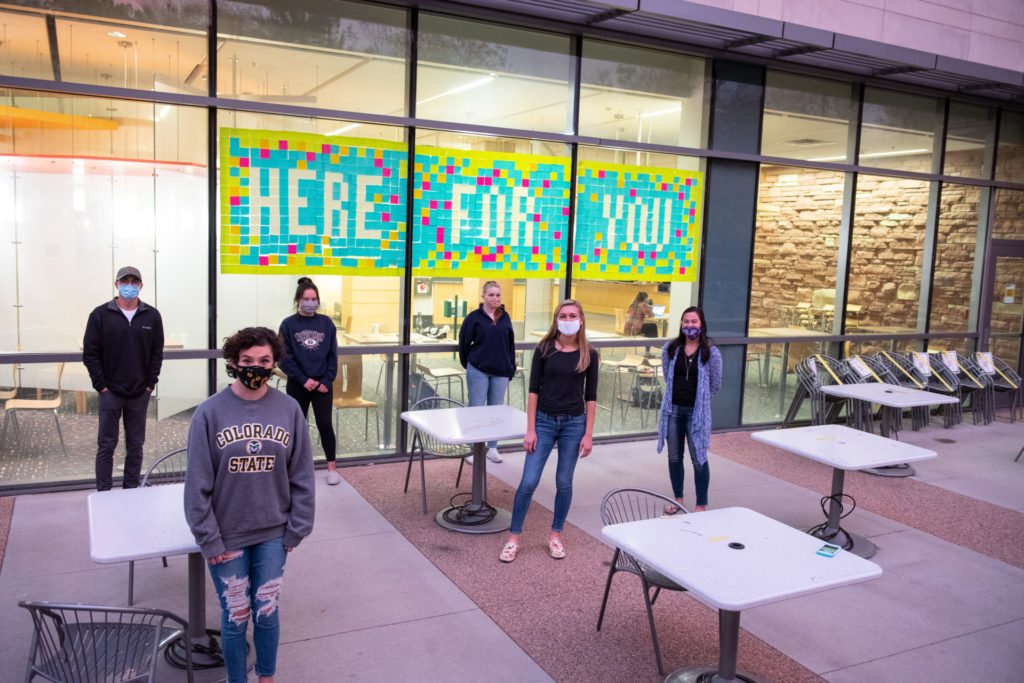 Members of Active Minds at Colorado State University create a mural of sticky notes spelling out "Here For You," the club's slogan, and hand-written positive messages, October 21, 2020, on a window in the Behavioral Sciences Building. Active Minds at CSU is a mental health advocacy organization that seeks to empower college students to speak openly about mental health and suicidal behavior in order to educate others and encourage help-seeking behaviors.