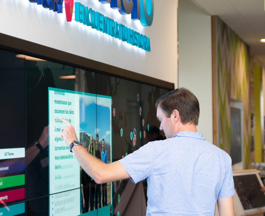 A person interacts with a large touch screen mounted on a wall.