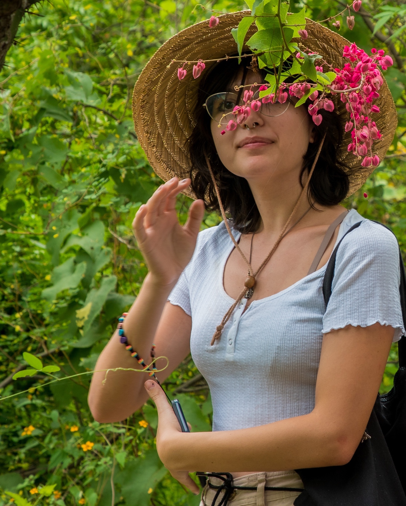 A young person wearing a straw hat looks at some pink flowers.