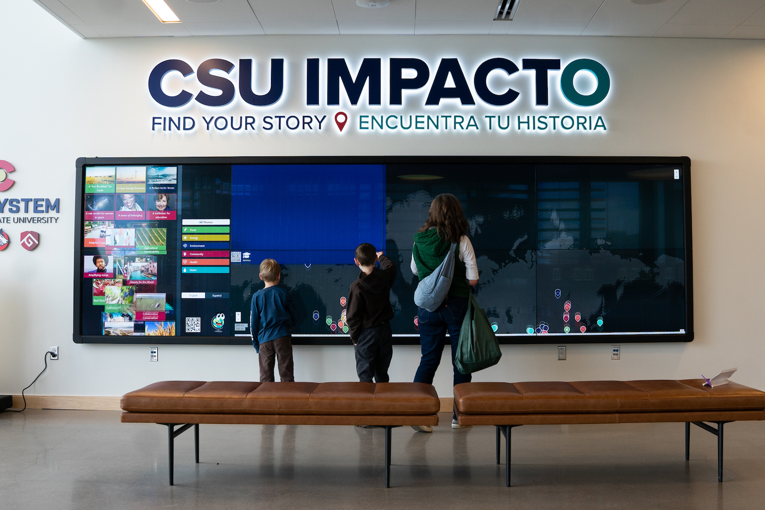 An adult and two children interact with a large wall-mounted map labeled CSU Impacto.
