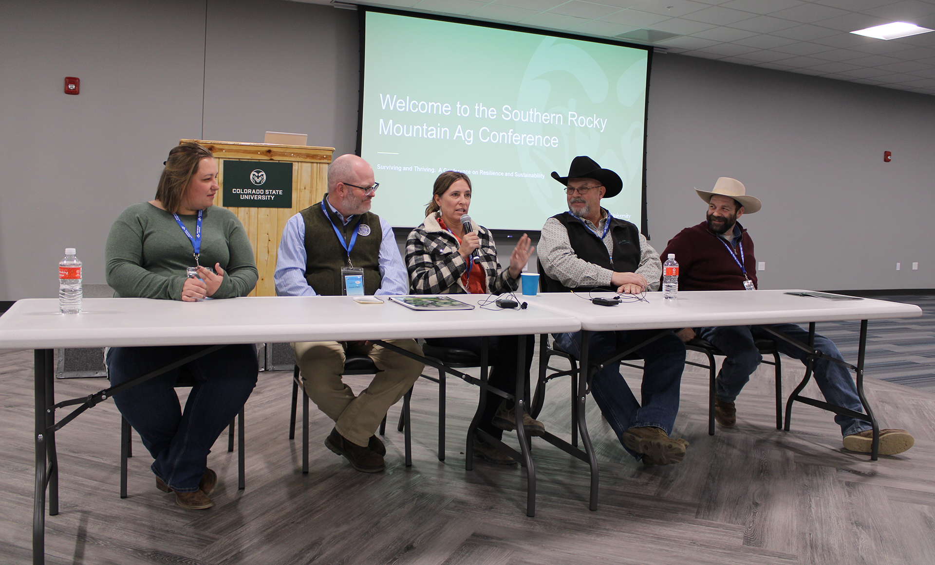 Five soil health experts sit at a table; center panelist speaks to audience using microphone