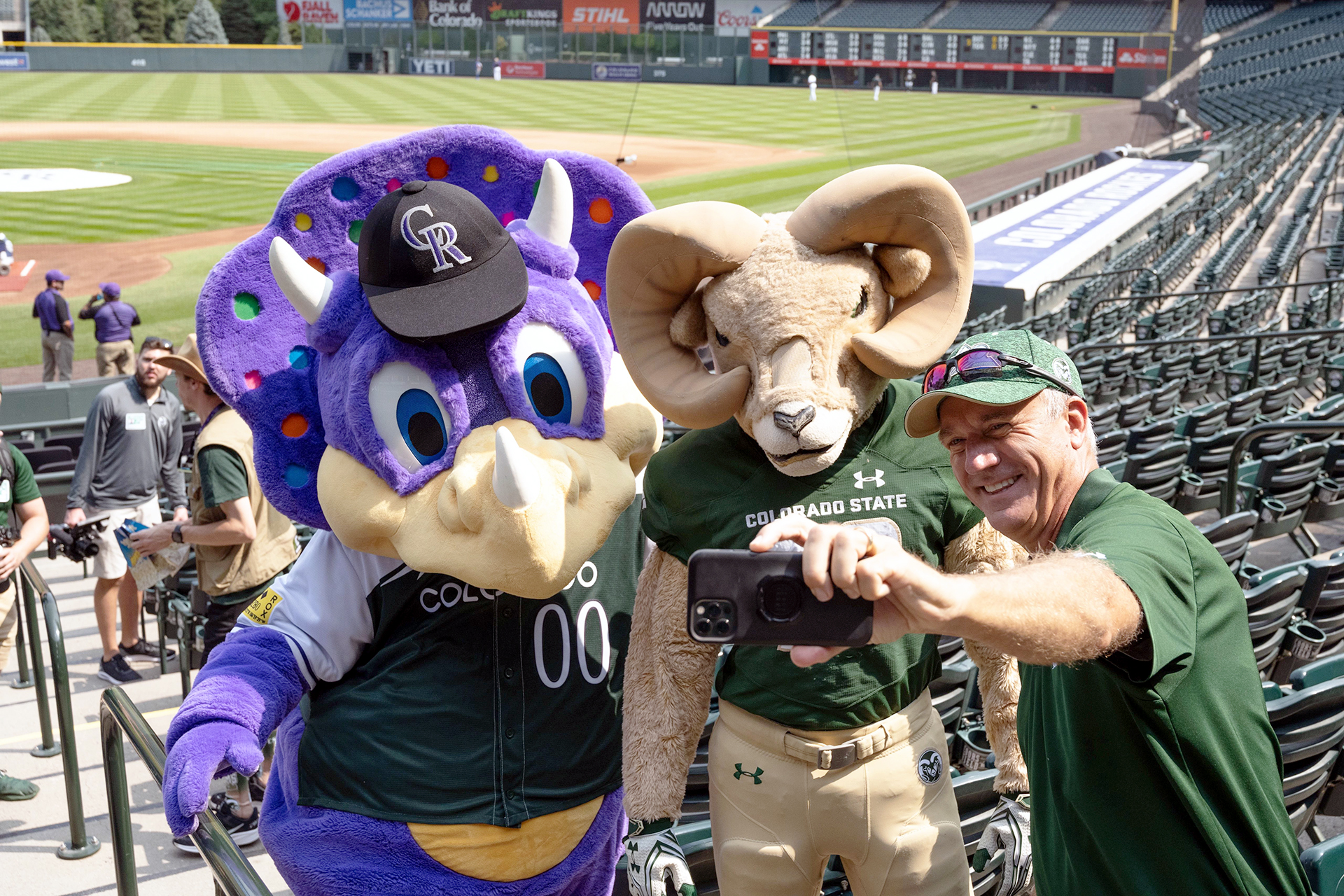 Rockies mascot Dinger and CAM the Ram pose for a selfie with a fan during the 2022 Rams at the Rockies baseball game.