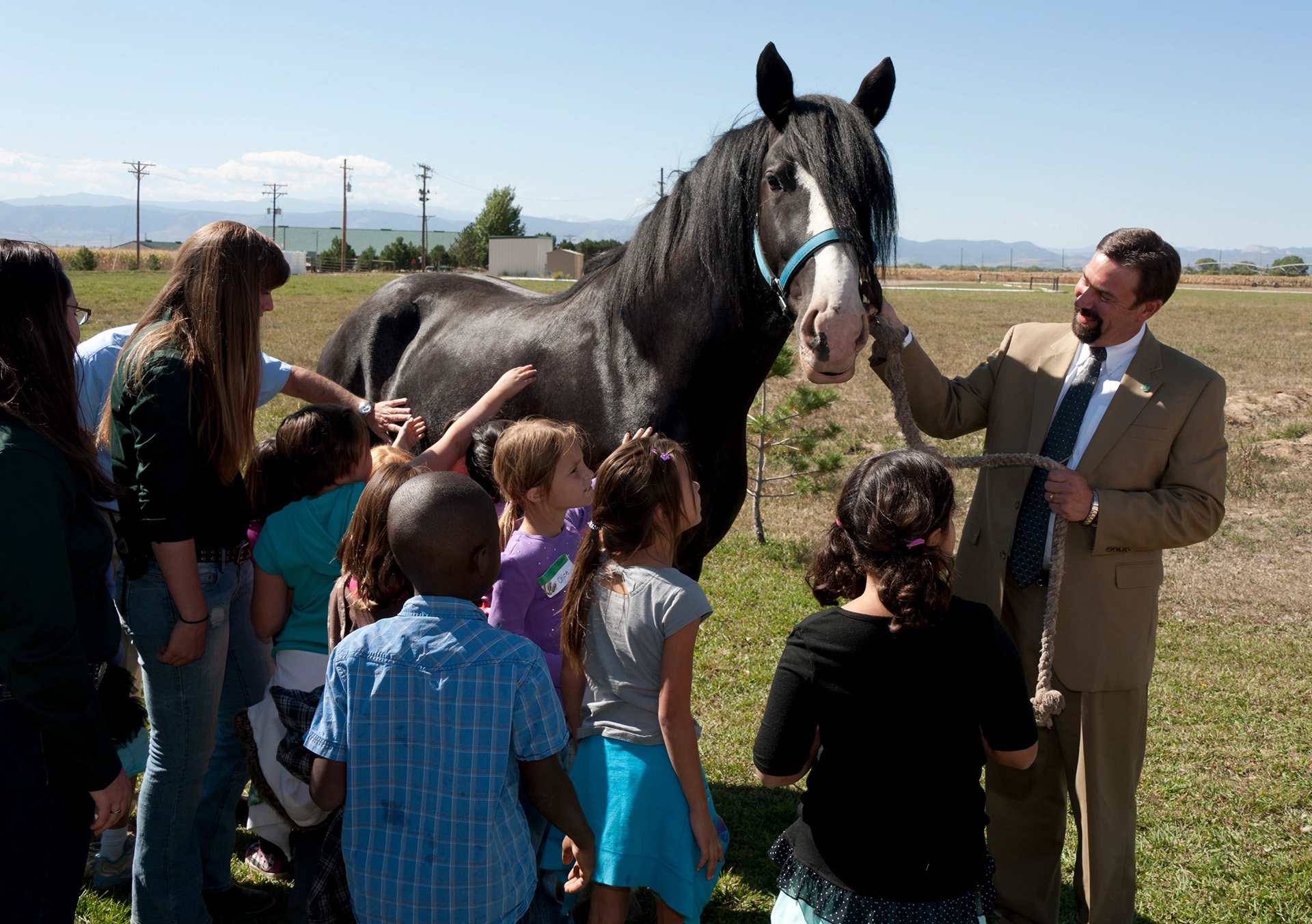 A man in a suit smiles and pets a horse while children stare in awe or pet the horse