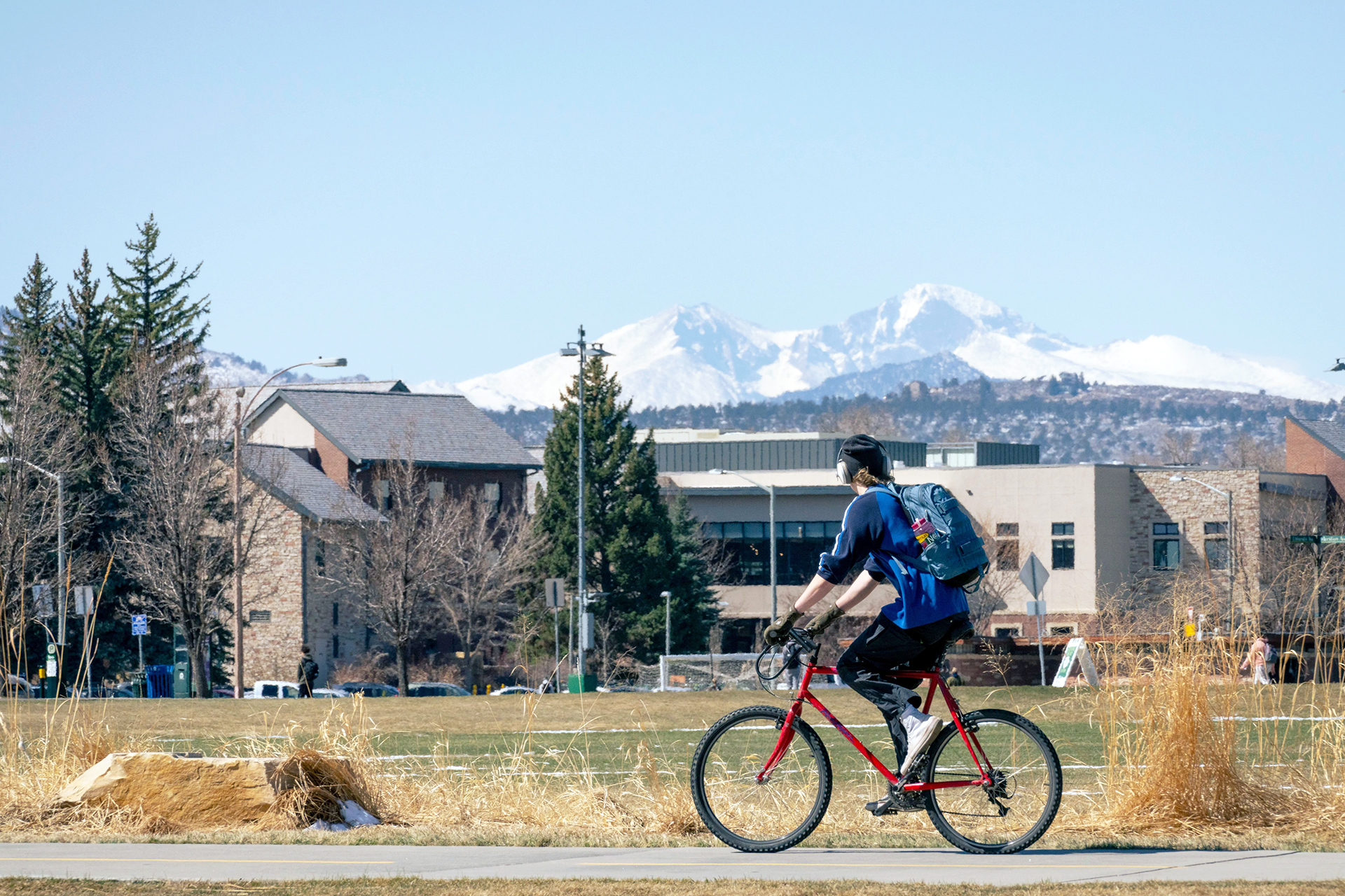 A student bicycles on the CSU campus with snow-capped mountains in the distance.