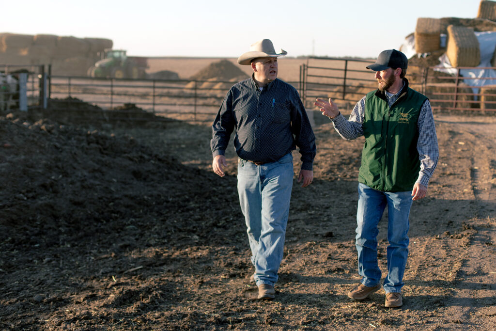 A CSU employee and farmer walk on the dirt at a farm.