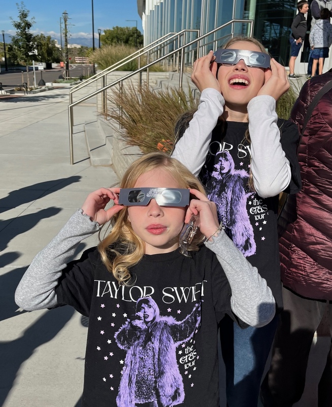 Two girls look at the sky through dark glasses.