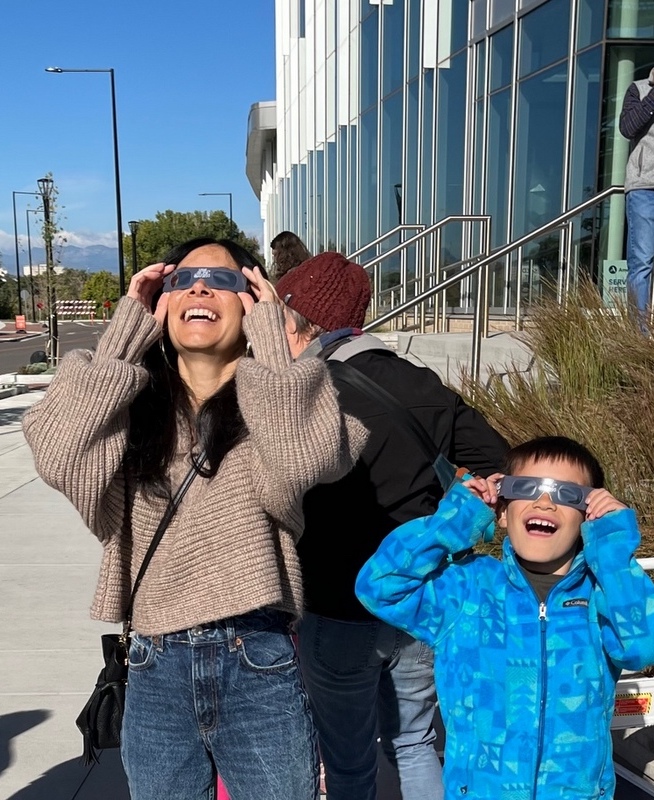 A woman and a boy look at the sky through dark glasses.