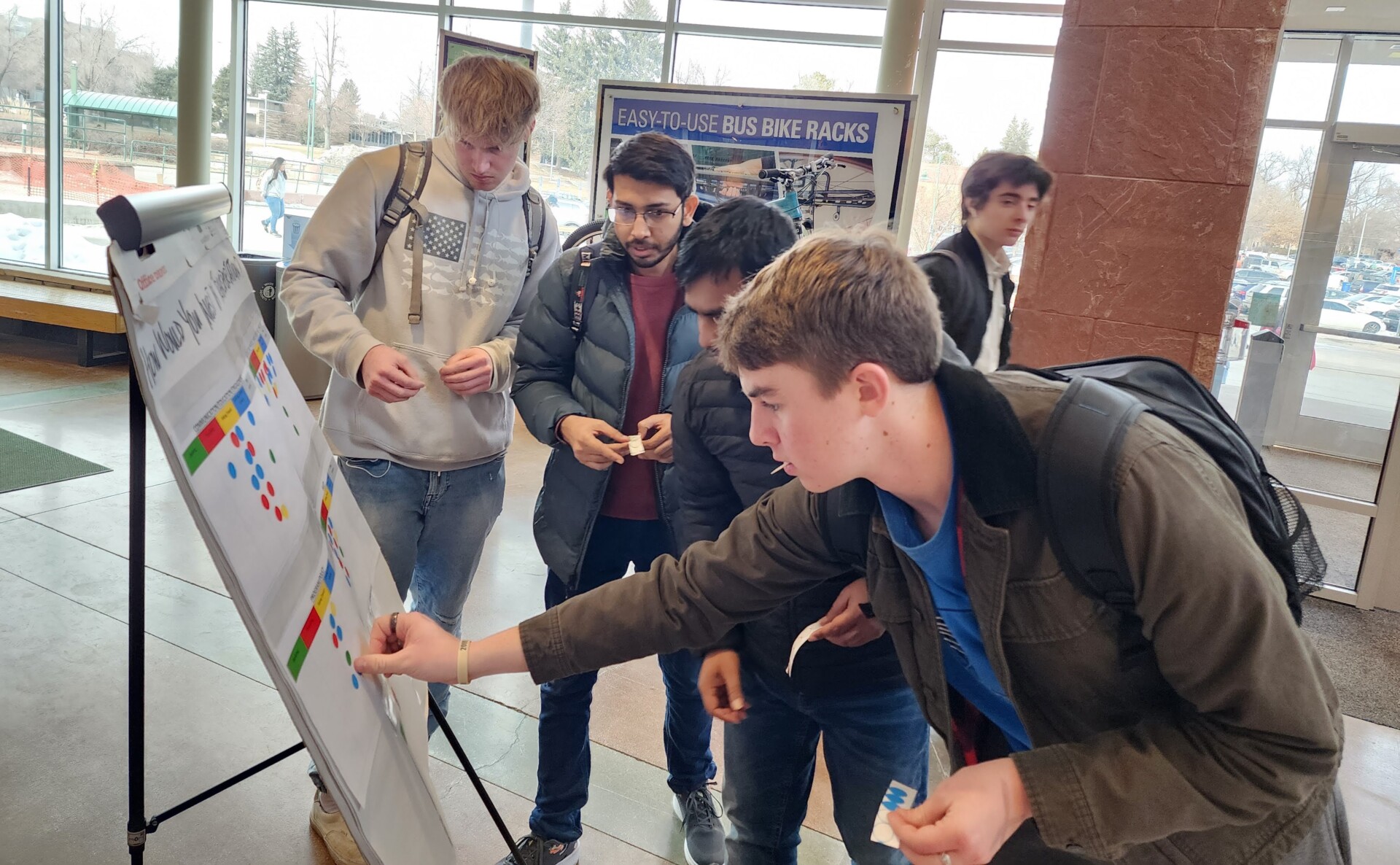 4 students stand in front an easel, placing stickers on a poster
