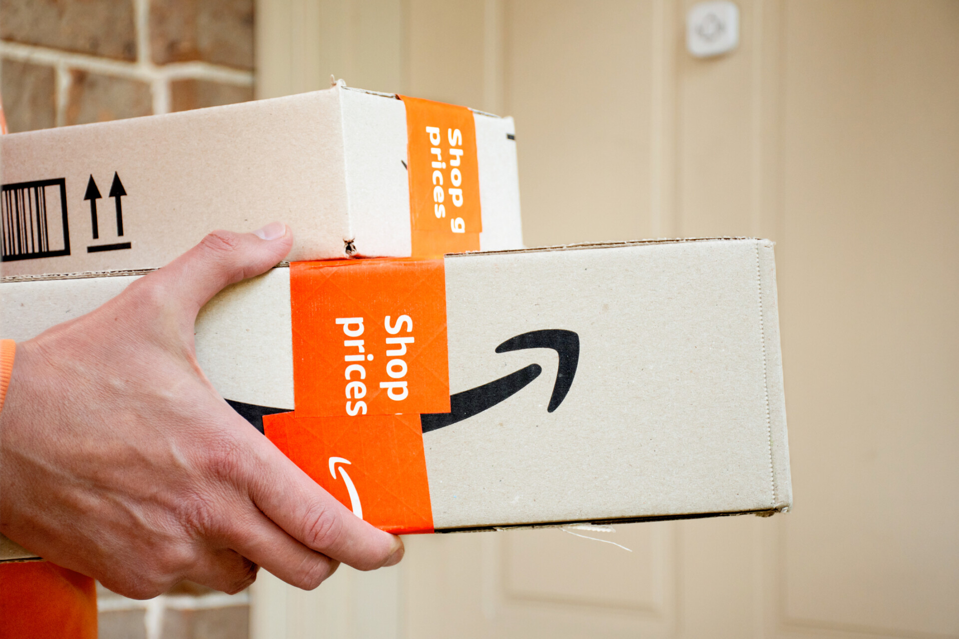 A hand holding two Amazon packages for delivery.