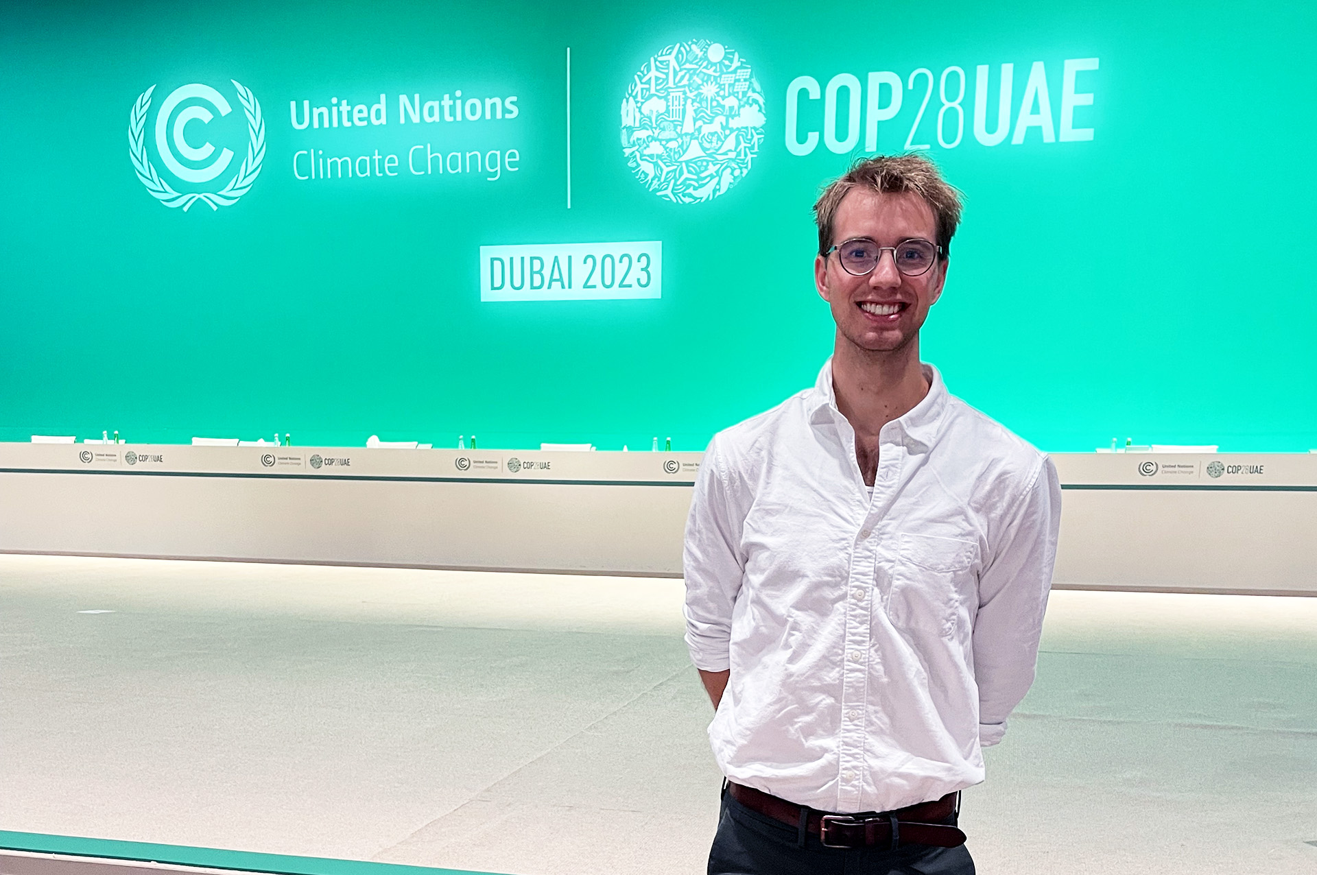 Colorado State University Ph.D. candidate Jacob VanderRoest stands in from of a bright aquamarine sign while at COP28 in Dubai in December 2023.
