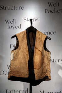 A brown vest displayed inside out shows a stain. It is part of the Avenir Museum's Spring 2024 exhibition.