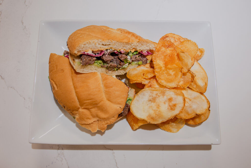 The Asada Torta, with choice of marinated skirt steak or a vegan, gluten-free patty, features guacamole, pickled onion, chipotle mayo, and queso fresco, and is served with homemade, seasoned potato chips.